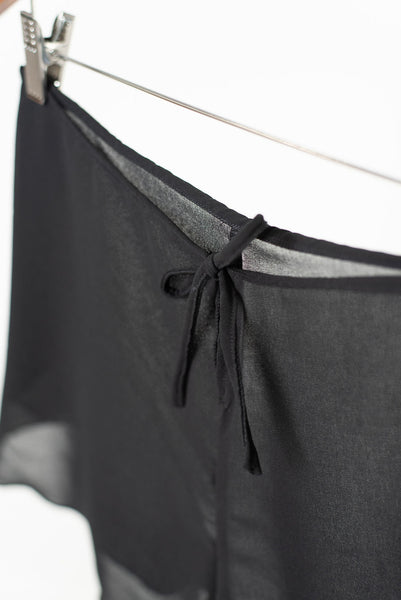 Detail view showing a tied bow at the back waist of a black pair of sheer chiffon shorts.