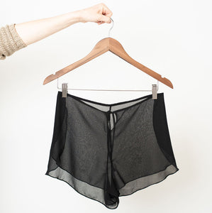 Pair of black sheer chiffon shorts on a wooden clip hanger.