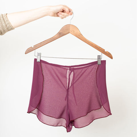 Pair of raspberry coloured sheer chiffon shorts on a wooden clip hanger.